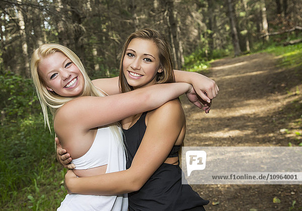 Zwei Freundinnen im Teenageralter umarmen sich auf einem Weg in einem Park und posieren für ein Foto; Edmonton  Alberta  Kanada'.