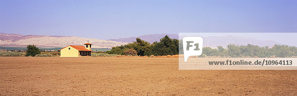 'A fallow field lies in the foreground with a country church  green fields and mountains beyond  Santa Ynez Valley; Lompoc  California  United States of America'