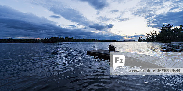 Silhouette eines Adirondack-Stuhls auf einem Holzsteg an einem See bei Sonnenuntergang; Ontario  Kanada'.