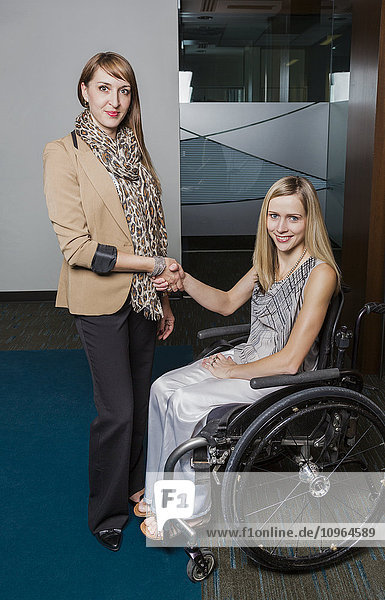 'A professional business woman shaking hands and posing with a young paraplegic woman in a wheelchair; St. Albert  Alberta  Canada'