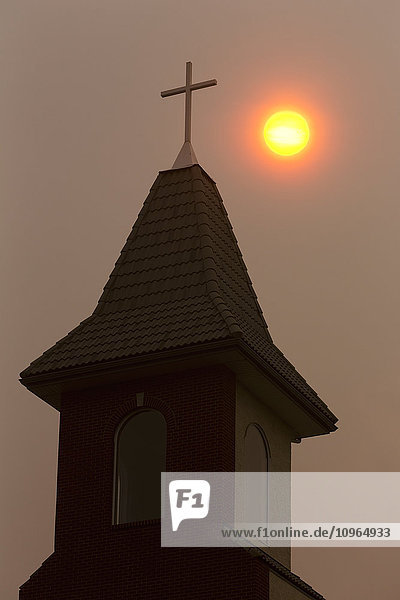 Silhouette eines Kirchturms mit orangefarbenem Sonnenball in einem dunstigen Himmel; Calgary  Alberta  Kanada