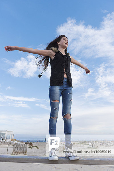 'A teenage girl stands on the rail of a fence with arms outstretched; Tarifa  Cadiz  Andalusia  Spain'