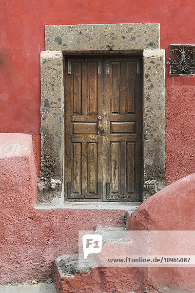 Abgenutzte Holztüren an einem rot gestrichenen Gebäude; San Miguel de Allende  Guanajuato  Mexiko'.