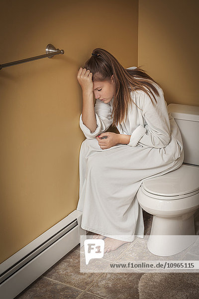 Teenager-Mädchen sitzt im Badezimmer auf dem Toilettensitz und schaut unglücklich