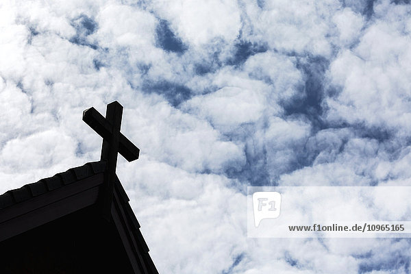 Silhouette eines Kreuzes auf dem Dach einer Kirche mit flauschigen Wolken und blauem Himmel; Calgary  Alberta  Kanada'.