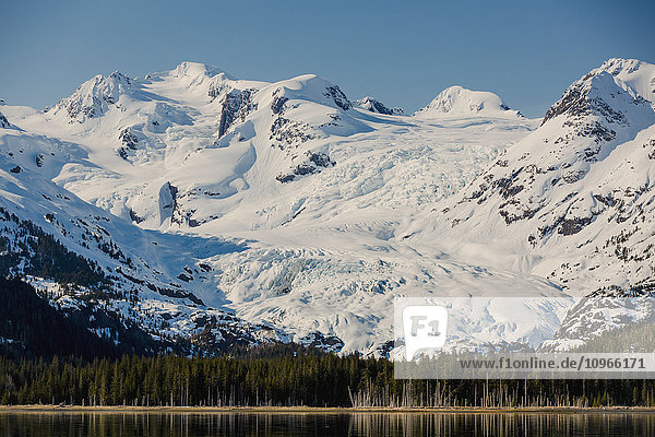 'A glacier hangs in a valley below jagged snow covered peaks in Kings Bay  Prince William Sound; Whittier  Alaska  United States of America'