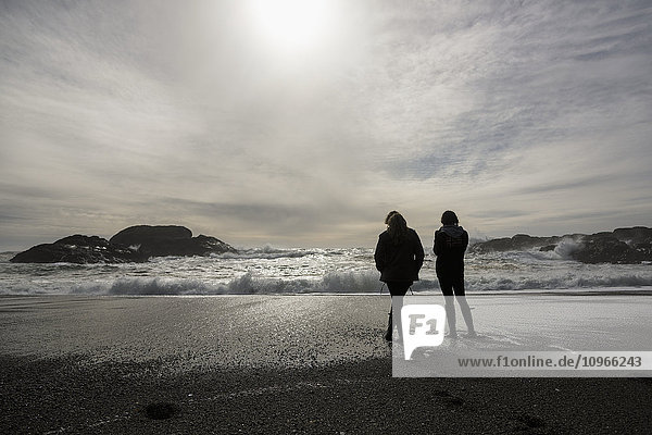 'Silhouettes two girls standing at the water's edge looking at the waves  Vancouver Island; Tofino  British Columbia  Canada'