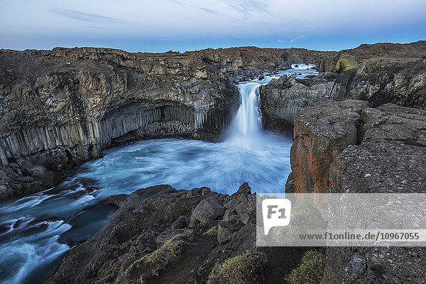 'The basalt column and waterfall known as Aldeyjarfoss in Northern Iceland a person stands at the top and photographs them; Iceland'