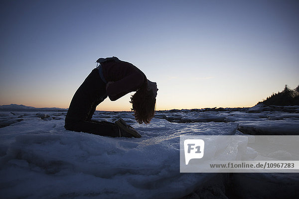 Woman practices yoga on an ice chunk on a beach in Homer  Southcentral Alaska
