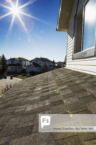 Nahaufnahme von brandneuen Dachschindeln mit Häusern in der Nachbarschaft  Sonne und blauem Himmel im Hintergrund; Calgary  Alberta  Kanada'.