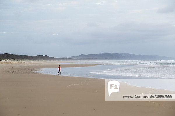 'Person walks towards the water on a beach along the Noose North shore under a cloudy sky; Noosa  Queensland  Australia'