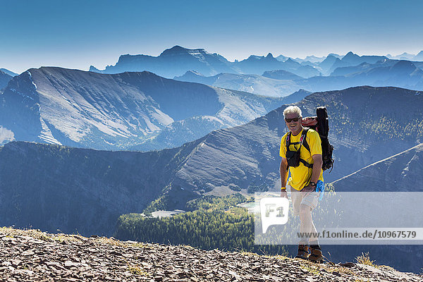 'Male hiker ascending a rocky peak with mountain ranges and lakes in the background; Waterton  Alberta  Canada'