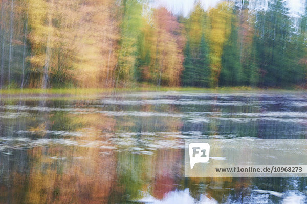 Unscharfe herbstlich gefärbte Bäume entlang der Uferlinie  die sich in einem ruhigen Fluss spiegeln; Ontario  Kanada'.
