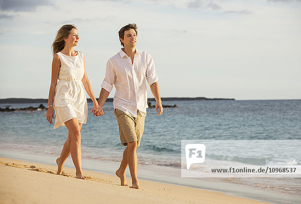 Romantic happy couple walking on beach at sunset. Smiling with arms around each other. Man and woman in love