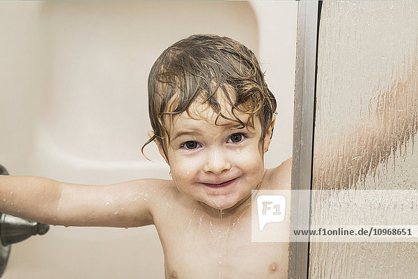 'Youngster smiling and peeking out from behind a glass shower door in a bathroom; St. Albert  Alberta  Canada'