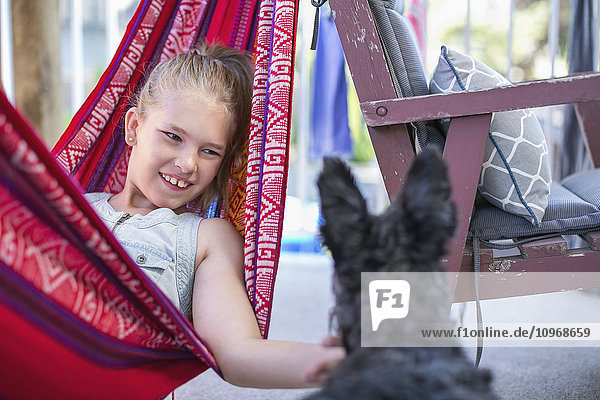 'Girl relaxing in a hammock and petting her dog; Langley  British Columbia  Canada'