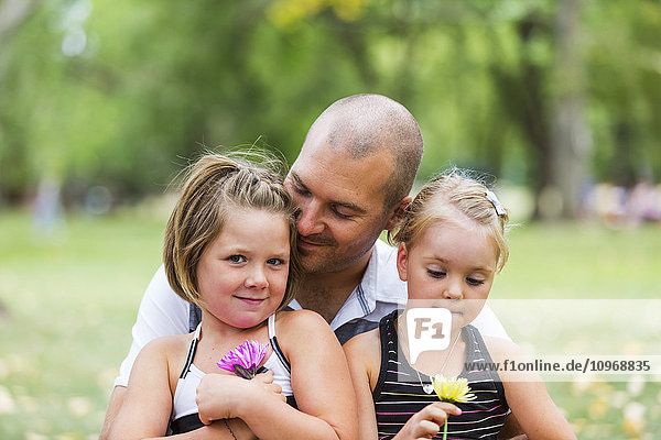 'A father holding his two daughters in a park; Edmonton  Alberta  Canada'