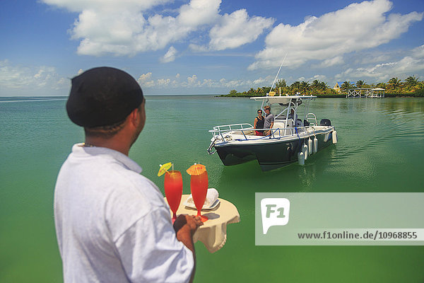 Ein Paar in einem Boot nähert sich einem Steg  an dem ein Kellner mit Getränken wartet  Saint Georges Caye Resort; Belize City  Belize'.