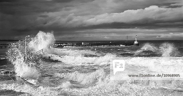 Wellen brechen an der Küste mit einem kleinen Leuchtturm am Ende eines Piers; Amble  Northumberland  England'.