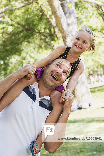 'Father carrying his daughter on his shoulders in a park; Edmonton  Alberta  Canada'
