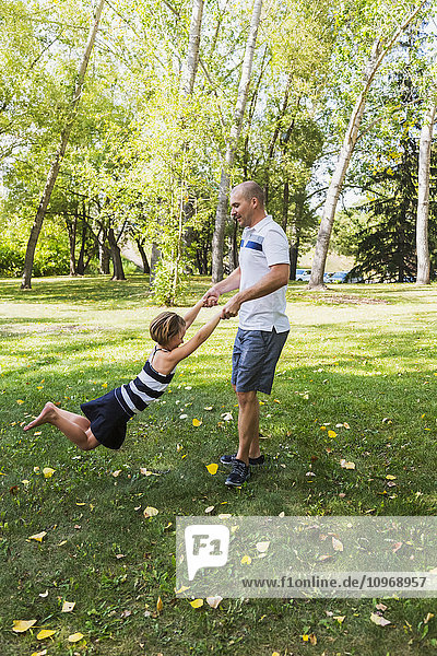 Ein Vater schaukelt seine Tochter während eines Familienausflugs in einem Park herum; Edmonton  Alberta  Kanada'.