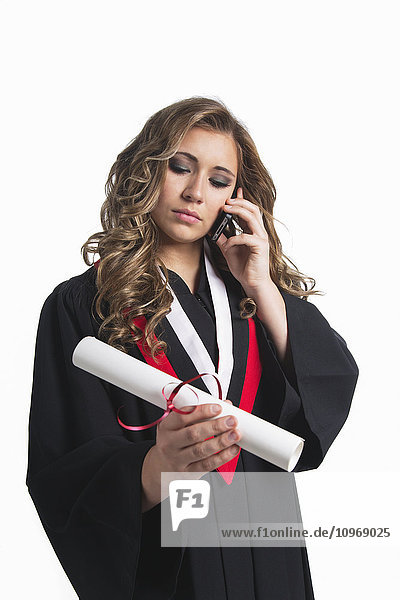 Junge Absolventin hält ihr Diplom in der Hand und telefoniert mit ihrem Smartphone; Edmonton  Alberta  Kanada'.