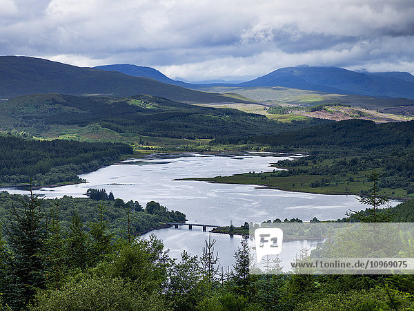 Fluss- und Waldlandschaft mit Bergen unter einem bewölkten Himmel; Schottland