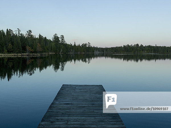 Hölzerner Steg  der bei Sonnenaufgang auf einen ruhigen See hinausführt; Whiteshell  Manitoba  Kanada'.