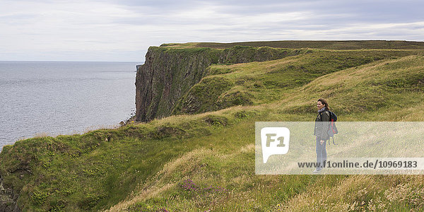 Eine Frau steht im Gras in der Nähe eines Bergrückens mit Blick auf Duncansby Head; John O'Groats  Schottland'.