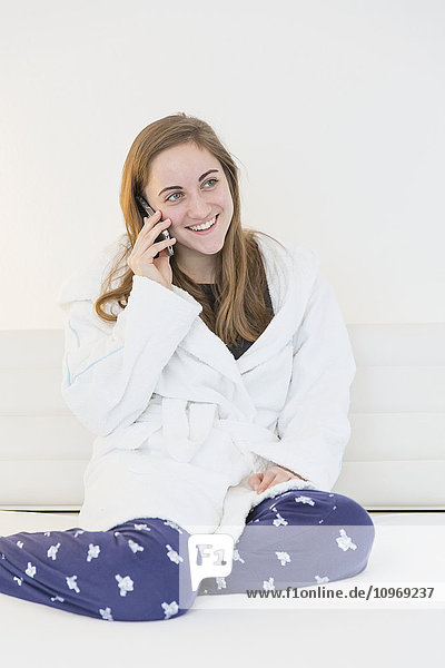 'A teenage girl wearing pajamas and robe sitting on a couch talking on a cell phone; Bonn  Nordrhein Westfalen  Germany'