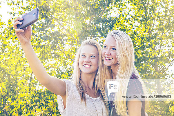 Zwei Schwestern  die im Herbst in einem Stadtpark Spaß haben und Selfies von sich machen; Edmonton  Alberta  Kanada'.
