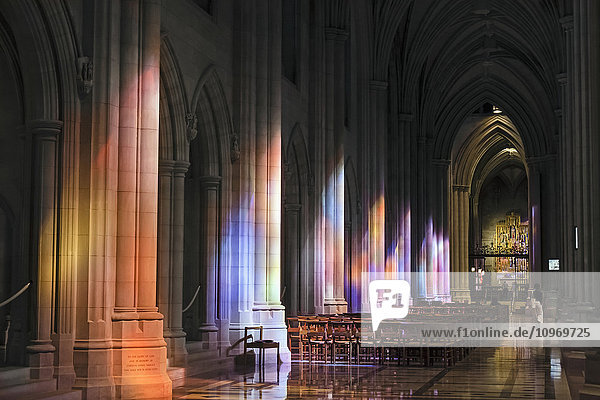 'Light streaming through stained glass windows with colourful light columns along the cathedral nave  altarpiece in St. Mary's Chapel visible background; Washington  District of Columbia  United States of America'