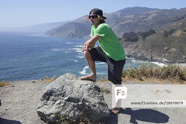 Ein junger Mann steht auf einem Bergrücken mit Blick auf den Ozean und die kalifornische Küste; Big Sur  Kalifornien  Vereinigte Staaten von Amerika'.