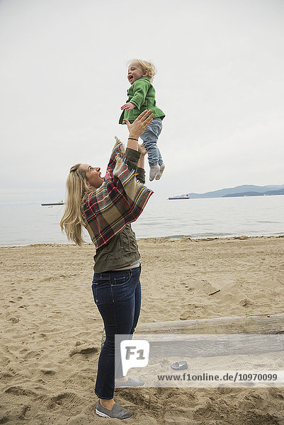In einer winterlichen Strandszene wirft eine Mutter ihr kleines Mädchen freudig in die Luft; Vancouver  British Columbia  Kanada'.