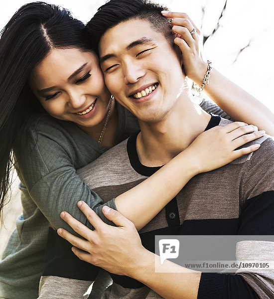 'A young Asian couple enjoying quality time together outdoors in a park in autumn and embracing each other in the warmth of the sunlight during the early evening; Edmonton  Alberta  Canada'