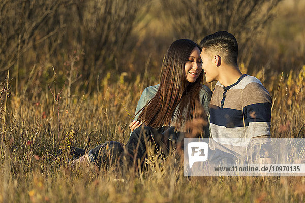 'A young Asian couple enjoying quality time together outdoors in a park in autumn in the warmth of the sunlight during the early evening; Edmonton  Alberta  Canada'