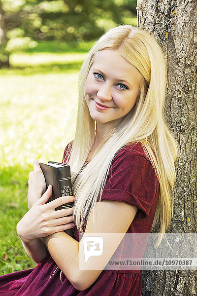 Eine junge Frau mit langen blonden Haaren hält ihre Bibel dicht vor der Brust  während sie eine persönliche Andacht in einem Park im Herbst hält; Edmonton  Alberta  Kanada'.