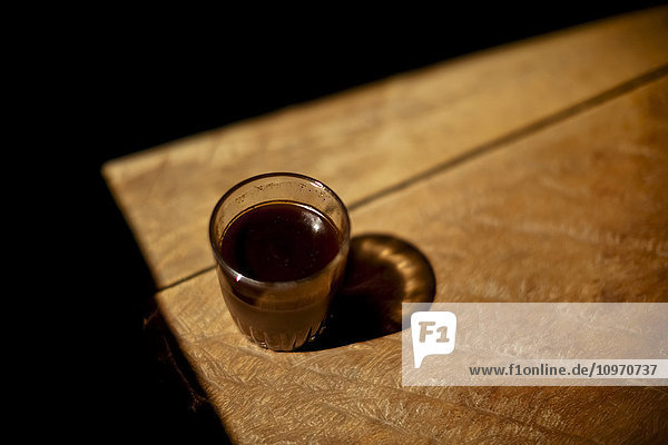 Ein Glas heißer Kaffee steht im Sonnenlicht  hergestellt aus Bohnen  die mit einem hölzernen Mörser geröstet und gemahlen wurden  keine 200 Fuß entfernt. Muara Pinang ist ein großes Kaffee produzierendes Dorf auf Sumatra  Indonesien.