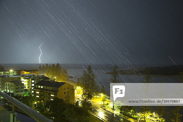 Ein Blitz schlägt in der Ferne in den Boden ein und Schlieren von Regen fallen; Caloundra  Queensland  Australien'.