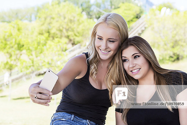 Zwei Freundinnen machen Selfies von sich im Freien in einem Stadtpark; Edmonton  Alberta  Kanada'.