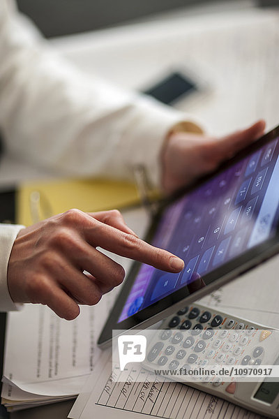 Eine Frau arbeitet an einem Tablet-Rechner an einem Schreibtisch mit Papierkram und einem manuellen Taschenrechner; Regina  Saskatchewan  Kanada'.