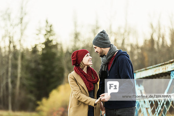 Ein junges Paar  das sich auf einer Brücke in einem Park im Herbst in die Augen schaut und die Hände hält; Edmonton  Alberta  Kanada'.