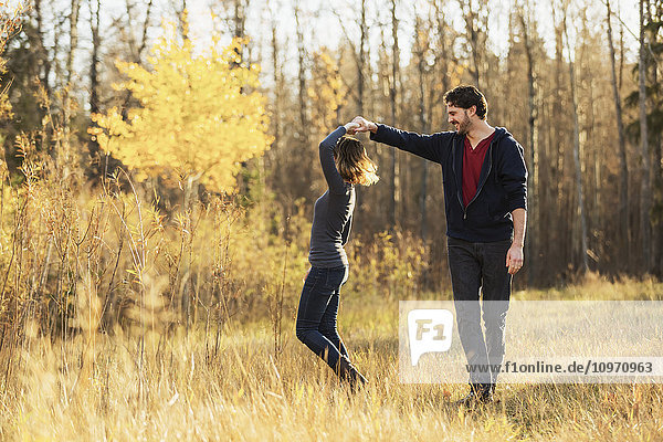 'A young couple walking and pretending to dance in a city park in autumn; Edmonton  Alberta  Canada'
