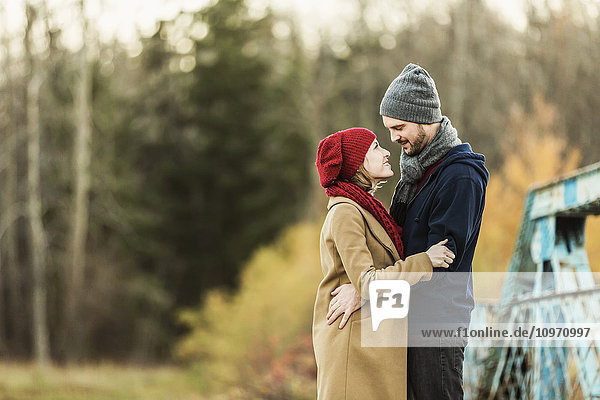 Ein junges Paar  das sich umarmt und in die Augen schaut  auf einer Brücke in einem Stadtpark im Herbst; Edmonton  Alberta  Kanada