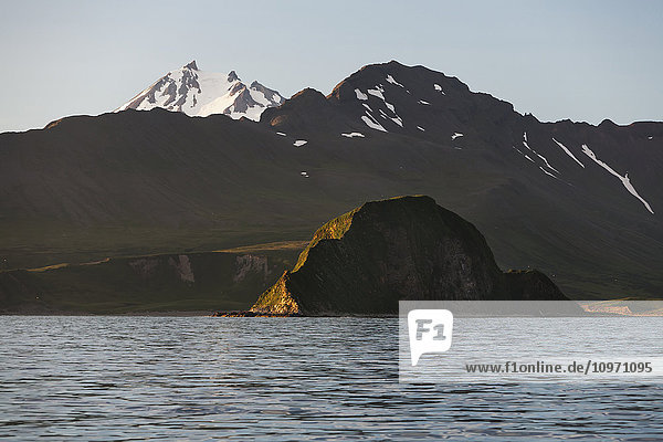 'Frosty Volcano Peaking Out From Behind A Ridgeline With Aagat Island In The Foreground Near Cold Bay On The Alaska Peninsula; Southwest Alaska  United States Of America'