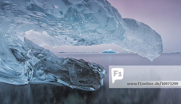 'Iceberg On The Beach Along The South Coast Of Iceland With A River Flowing By It Leading Towards The Ocean; Iceland'