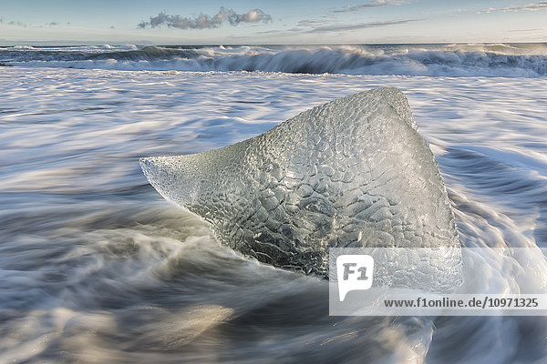 Kleiner Eisberg umgeben von fließendem Wasser entlang der Südküste Islands mit großen Wellen  die gegen die Küstenlinie schlagen; Island