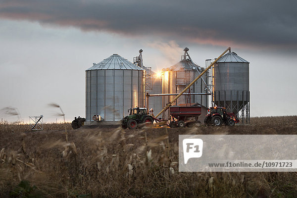 Getreidesilos und Traktor unter einem dramatischen Himmel bei Sonnenuntergang; Quebec  Kanada