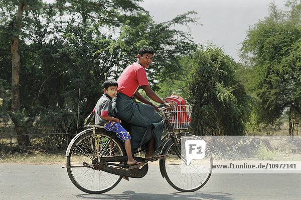 Ein Vater und sein kleiner Sohn fahren mit dem Fahrrad die Straße entlang; Bagan  Myanmar'.