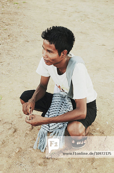 'A boy crouches on a dirt ground; Bagan  Myanmar'